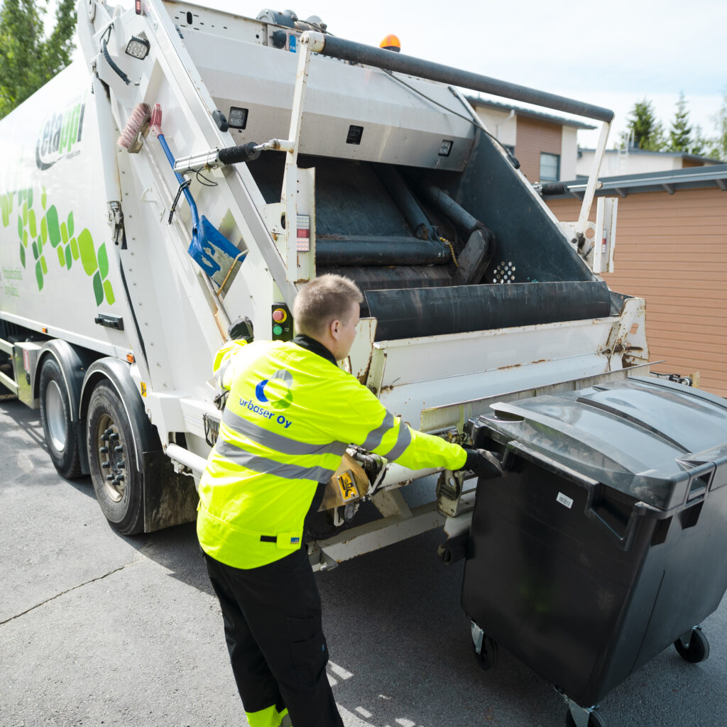 Jätteenkuljettaja tyhjäämässä jätesäiliötä jäteautoon.